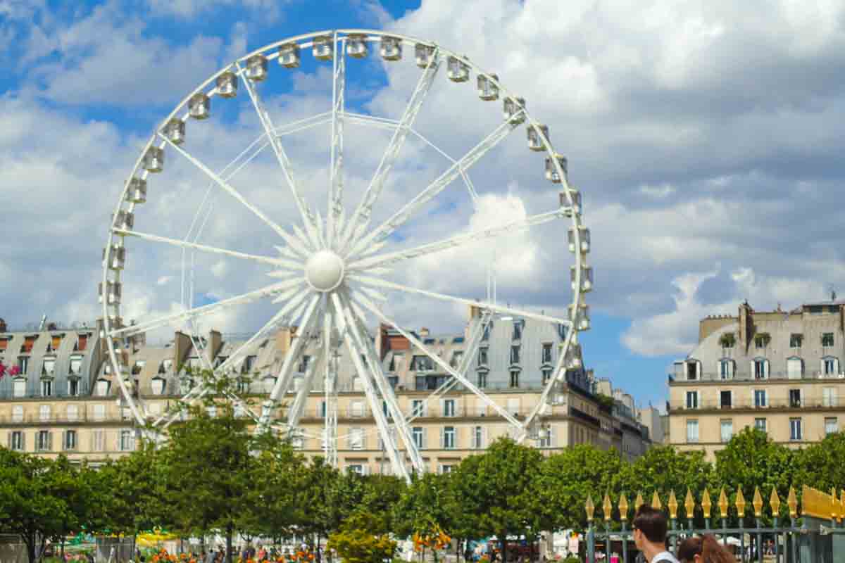 A large Ferris wheel stands in an urban area with historic buildings in the background.