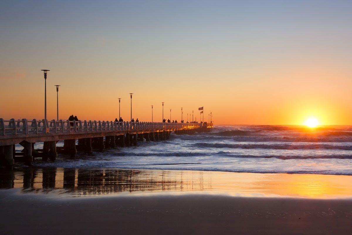 A long pier extends over the ocean at sunset.