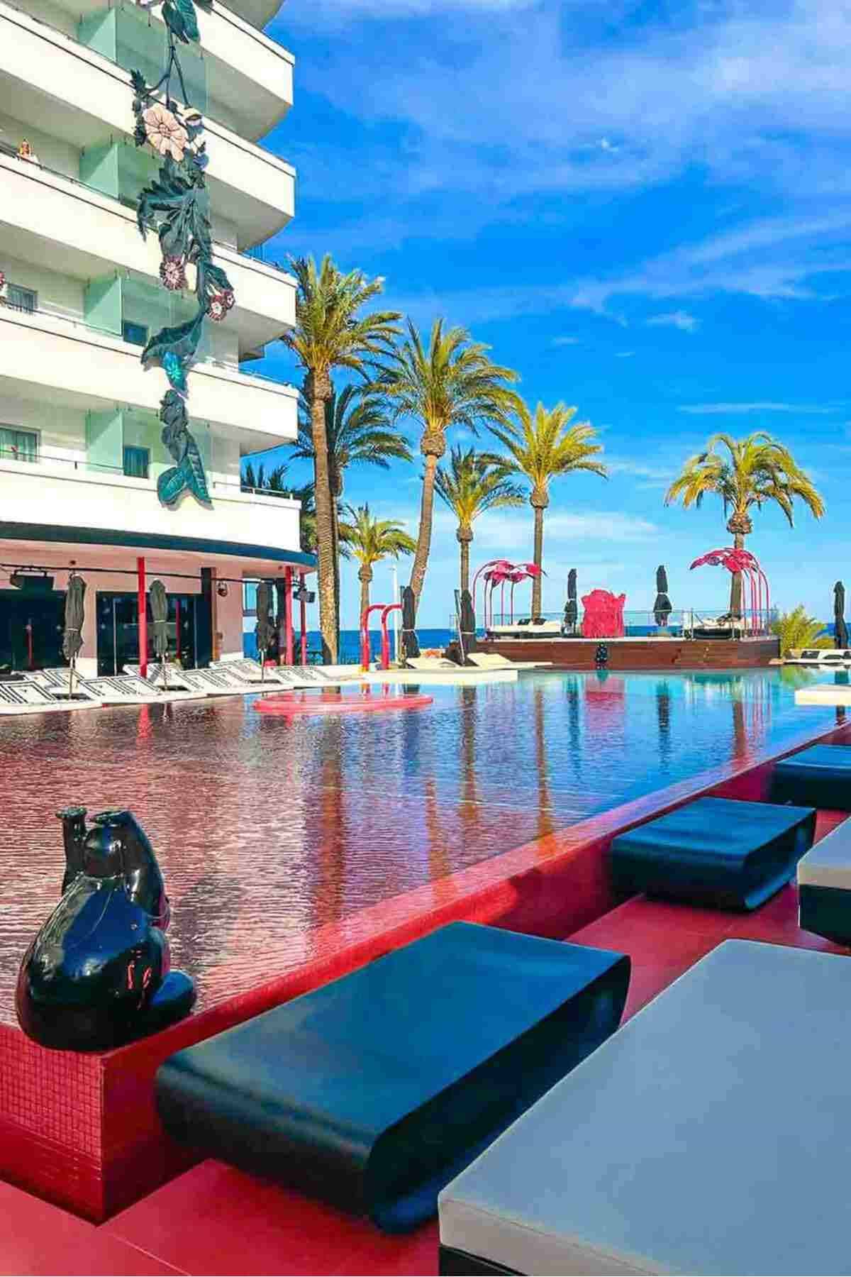 Modern hotel with poolside lounge beds and palm trees.