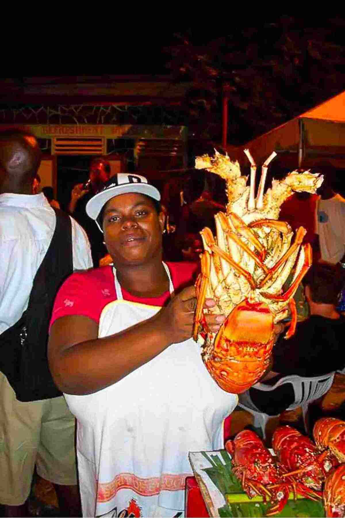 Person holding a large lobster at a bustling outdoor market.