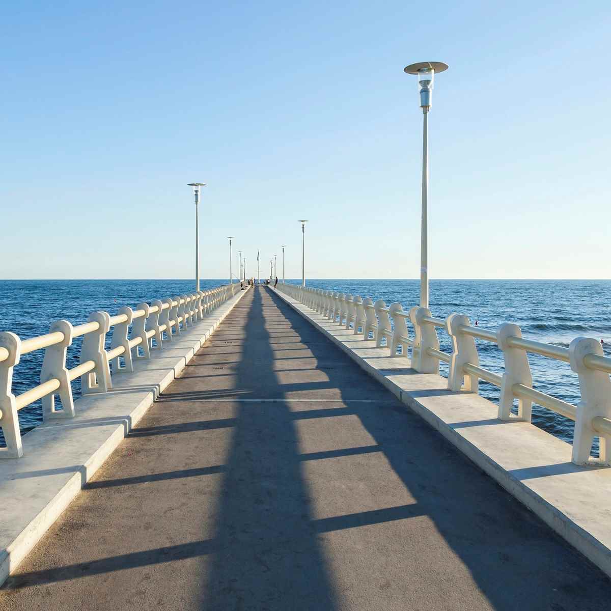 A long concrete pier with lampposts extends into the sea.