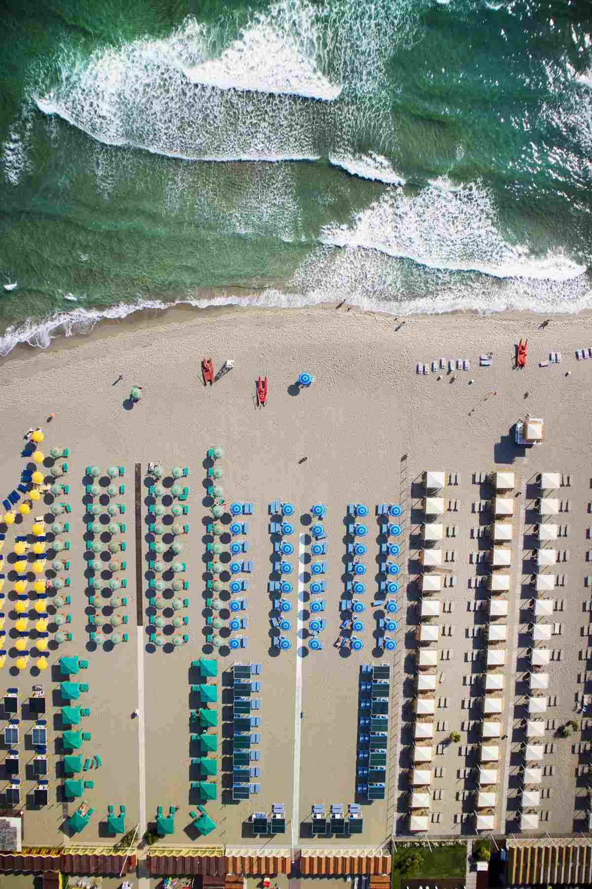 Aerial view of a beach with rows of colorful sun umbrellas and loungers.